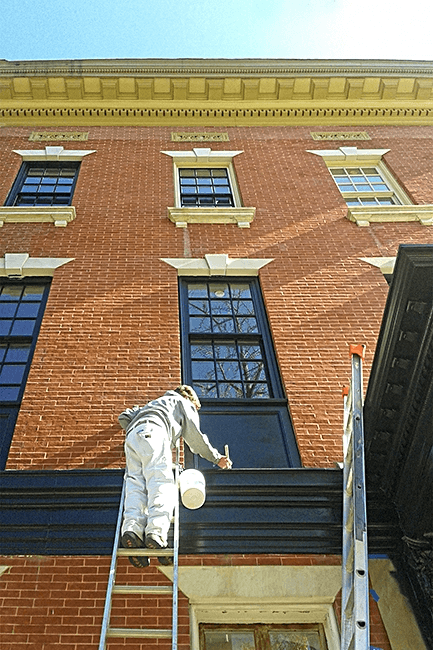 Heritage Hills Painting Restoration lady on ladder painting small building